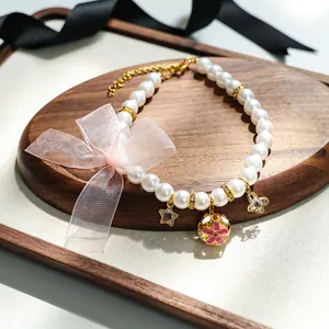 Détail du collier de perles pour animaux avec nœud rose et clochette dorée