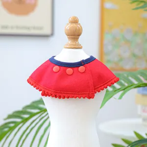 Detail of red pet cape with decorative pompoms and navy blue collar on mannequin