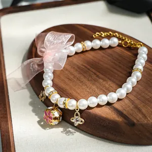 Détail du nœud en organza rose, cloche dorée et pendentif papillon sur collier de perles