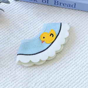 Detail of light blue pet bib with yellow duck embroidery and white wavy lace trim