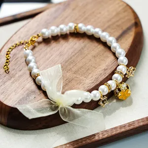 Détail de collier perles pour animaux avec nœud en tulle, breloques dorées et fermoir mousqueton