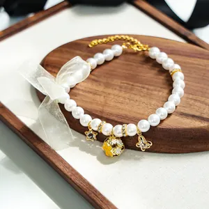 Détail du collier de perles pour animaux avec breloques dorées et nœud blanc