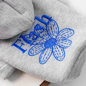 Detaillierte Makroansicht der blauen Gänseblümchen-Stickerei auf grauem Strick-Haustierpullover