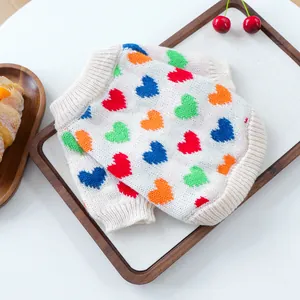 Detalle de suéter tejido para mascotas con coloridos corazones pixel sobre crema