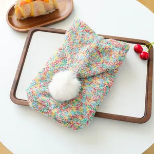 Detail of colorful knitted pet sweater featuring a soft white faux fur pom-pom detail