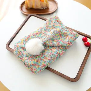 Close-up of colorful knitted pet sweater featuring a large fluffy white pom-pom detail