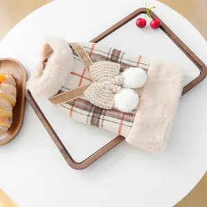 Detail of plaid pet vest featuring plush fur collar and white pom-pom decorations