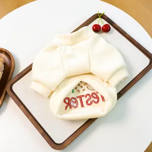 Detailed close-up of cream ribbed pet sweater with red embroidery on a wooden tray