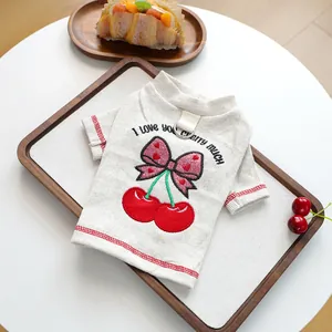 Detail of cherry embroidery and metal D-ring on a cream ribbed pet sweater vest