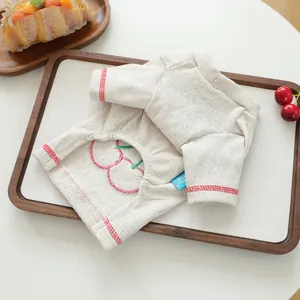 Texture détaillée du pull beige pour animaux avec broderie cerise et bordure rouge