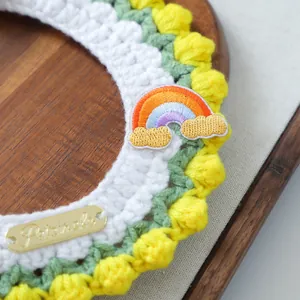 Detail of hand-knitted pet scarf with green scalloped edges and rainbow embroidery