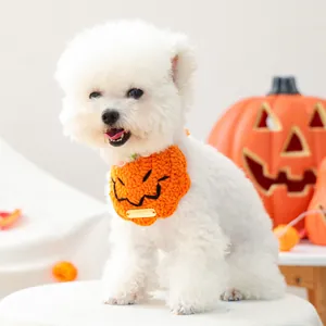 Detail van handgebreide oranje pompoen slabbetje met gouden logo op een witte hond