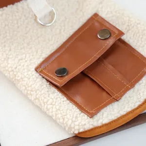 Close-up of fluffy white fleece pet vest featuring a brown faux leather pocket and D-ring