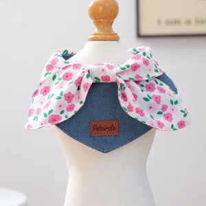 Detail of denim pet bandana featuring a pink floral bow and leather brand tag