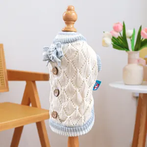 Detail of hollow knit pet sweater with light blue bow and wooden buttons on cream fabric