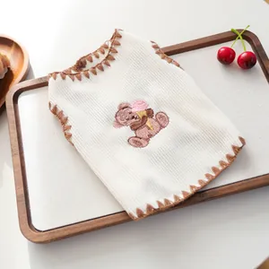 Detail der cremefarbenen Hundeweste mit Bärenstickerei und braunem Wellensaum