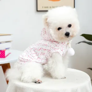Detail of pink floral pet hoodie with white pompom drawstring on a white dog