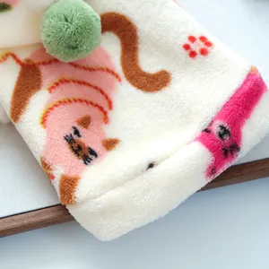 Detailed close-up of beige fleece pet clothes with cat print and green plush ball decor