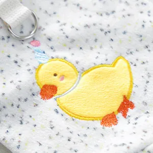 Close-up of white plush fabric with yellow duck embroidery and a metal D-ring attachment