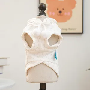 Detail of cream pet hooded vest featuring soft plush pom-poms and subtle speckled pattern