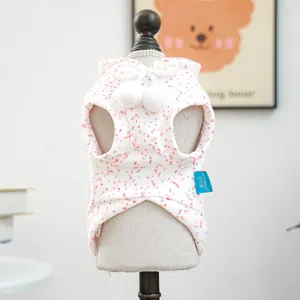 Close-up of a white pet vest with soft floral fabric and decorative plush pom-poms