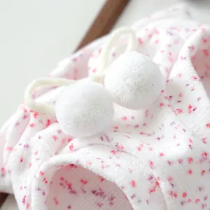 Close-up of soft white fleece pet hoodie with pink floral patterns and plush pom-poms