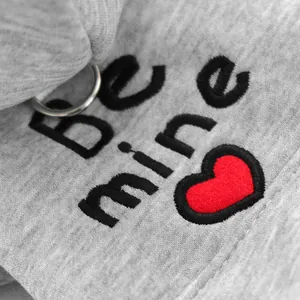 Detalle de sudadera gris para mascotas con bordado Be Mine e icono de corazón rojo