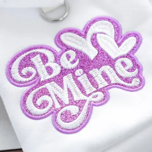 Detalle del bordado Be Mine con lentejuelas rosas y anillo en D en sudadera blanca para perro