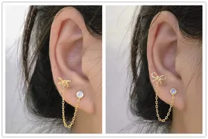 Detail of s925 silver double piercing chain earring with gold bow and purple zircon