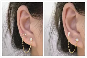 Detail view of double piercing chain earrings in gold plating with heart and zircon accents