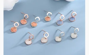 Detail of geometric silver and rose gold stud earrings with marbled enamel square charms