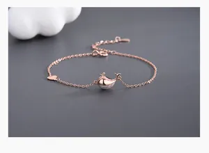 Detail view of rose gold whale bracelet with matte finish and heart charm on dark grey base