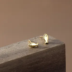 Minimalist gold fish stud earrings with tiny white zircon eyes on dark wood block