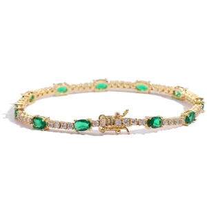 Detailed view of oval green emerald stones and round cubic zirconia on a gold tennis bracelet
