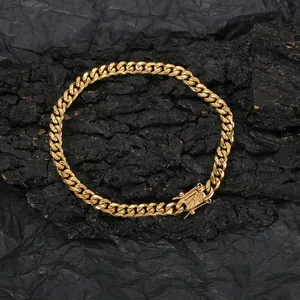 Detail of gold-plated Cuban link anklet with secure box clasp on a dark textured background