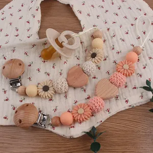 Detail of wooden pacifier clip and silicone nipple on floral bib with wood background
