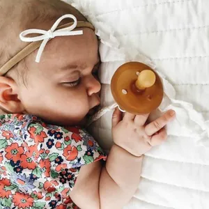 Tan silicone pacifier with white braided clip chain and matching bow headband on a sleeping baby