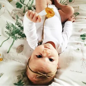 Close-up of brown braided leather pacifier clip attached to a baby cotton romper