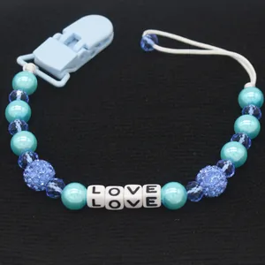 Detail of blue baby pacifier clip with pearls and white LOVE letter beads on black fabric