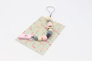 Detail of baby pacifier clip featuring silicone beads and wooden heart on flamingo card