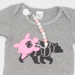 Pink silicone baby pacifier clip with turtle teether and beads on a grey baby onesie