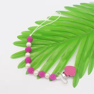 Detail view of baby pacifier clip with pink matte beads and white pearls on palm leaf