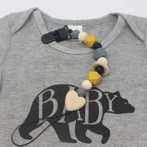 Silicone and wood baby pacifier clip with heart bead on a gray baby bodysuit