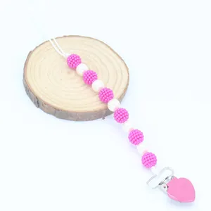 Pink and white pearl pacifier clip with heart metal clasp on a wooden base