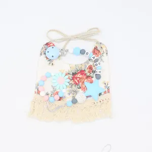 Flat lay of floral cotton baby bib and silicone pacifier clip with BABY letter beads