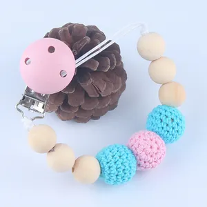 Roze houten fopspeenketting met blauwe gehaakte kralen en dennenappeldecor op de achtergrond