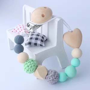Close-up of wooden pacifier clip with silicone beads and crochet textures on a mini bench
