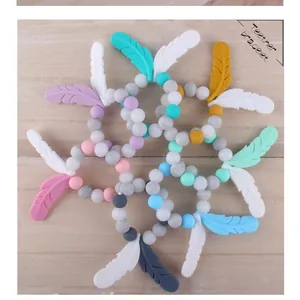 Close-up of colorful silicone teether bracelets with feather charms on a wood surface