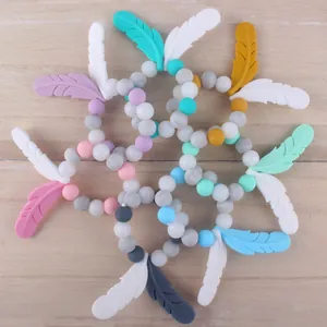 Beißringe aus Silikon für Babys mit Federanhängern in bunten Macaron-Farben auf Holz