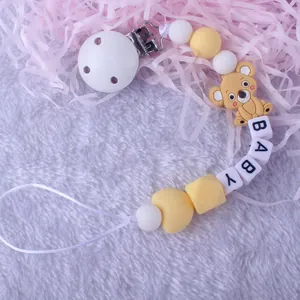 Detalle del sujetachupetes de silicona amarilla con clip de madera y letras BABY